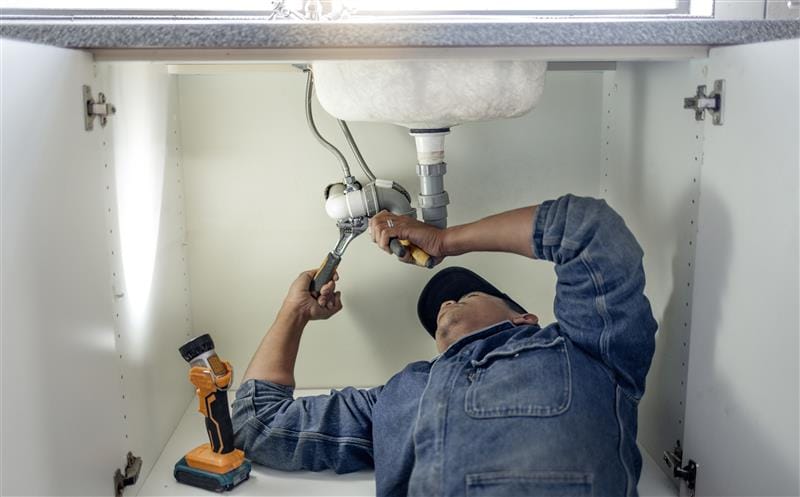 Plumber repairing pipes beneath a bathroom sink in North Fort Myers