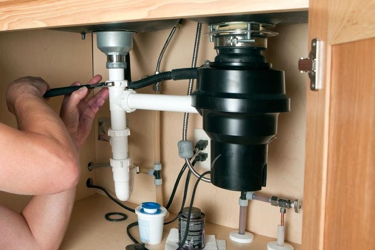 Plumber installing a garbage disposal beneath a kitchen sink in North Fort Myers