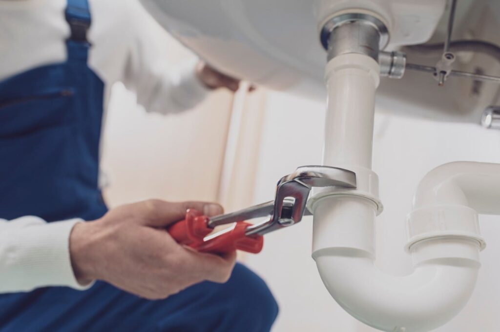 Plumber repairing a white drain pipe beneath a sink in North Fort Myers
